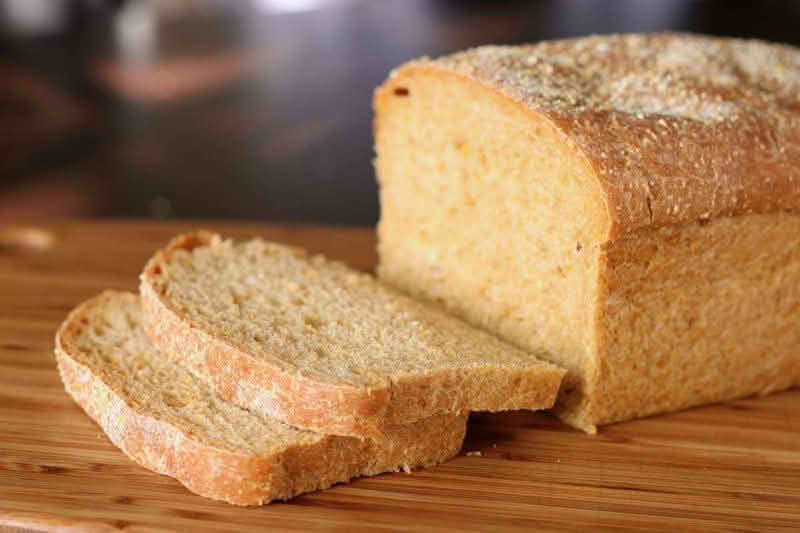 A loaf of anadama bread resting on a wooden cutting board, showcasing its rustic texture and golden-brown crust