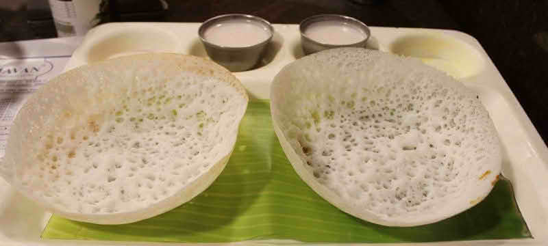 Two Appam pancakes served with coconut milk arranged neatly on a tray