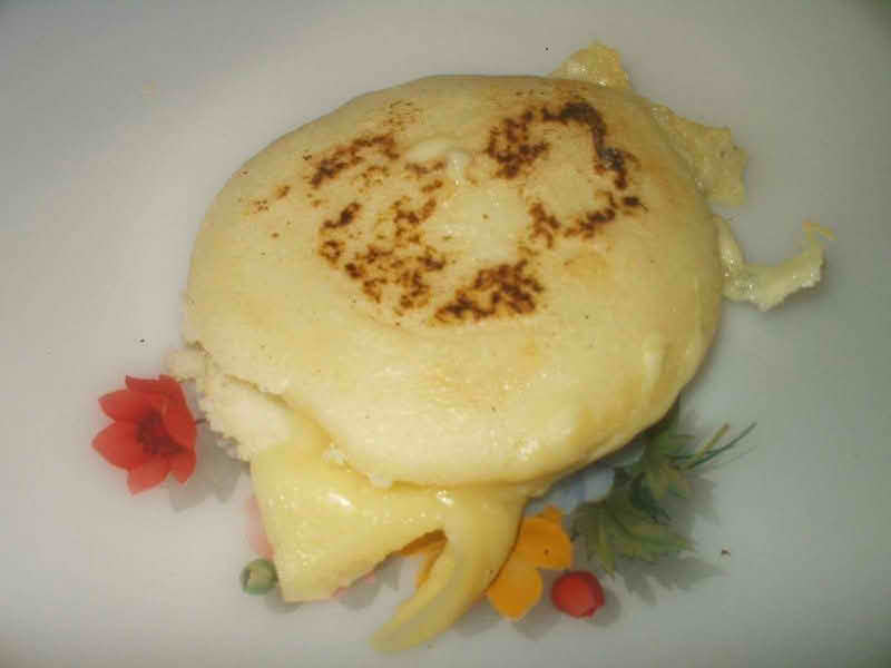 A plate featuring a golden arepa, a traditional cornmeal dish, with a cheese filling, garnished and ready to be enjoyed