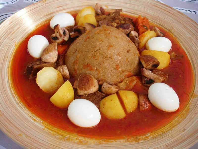 A plate of Bazin (center) served with a stew and whole hard-boiled eggs