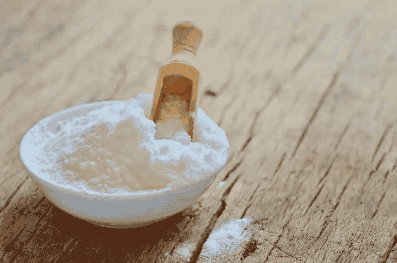 A bowl of baking soda with a wooden spoon resting on top, ready for use in baking or cooking