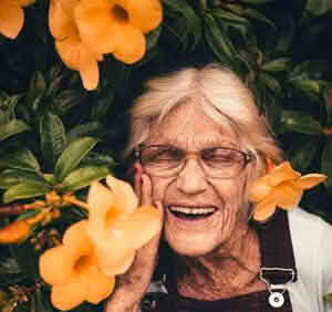 Roberta Johnson smiling with eyes closed near a plant with orange flowers