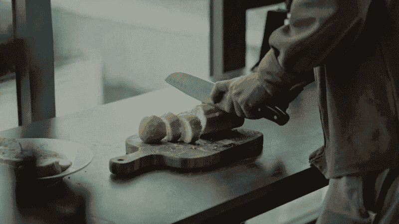 Close-up short looping video of someone slicing a baguette on a bread board